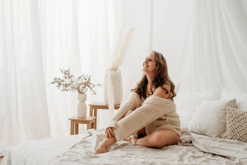 Lachende Frau mit Wollpullover sitzend am Bett