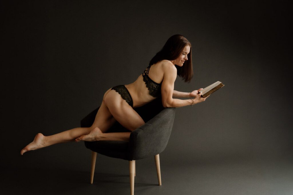 Sportliche Frau in Dessous kniet am Stuhl und liest ein altes Buch