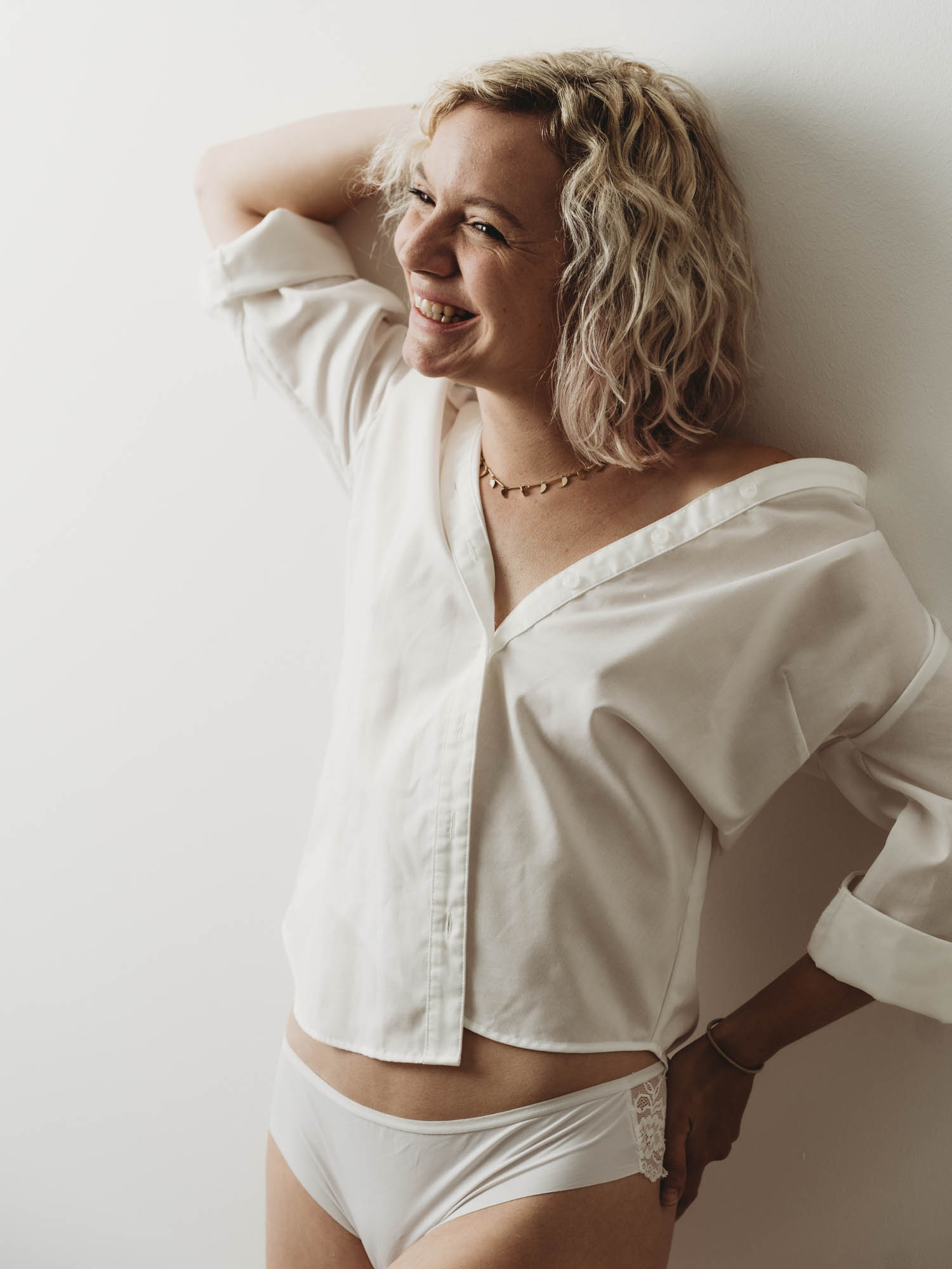 Boudoir Fotografie in Graz – Frau im weißen Hemd voller Leichtigkeit Lächelnde Frau im weißen Hemd während eines Boudoir Shootings in Graz.