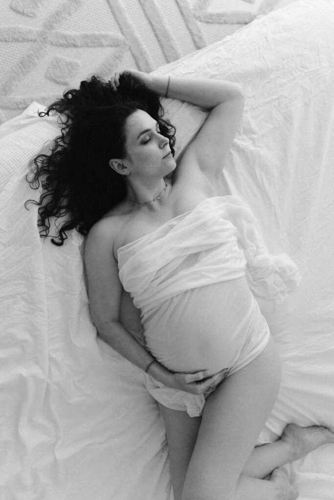 Schwangere Frau mit durchsichtigem Tuch liegend im Bett